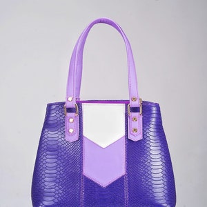May include: A purple and white handbag with a snakeskin pattern. The bag has two top handles and a zipper closure.