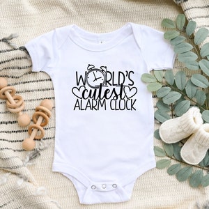 May include: White baby onesie with black text that reads "World's Cutest Alarm Clock" with a clock and heart graphic.