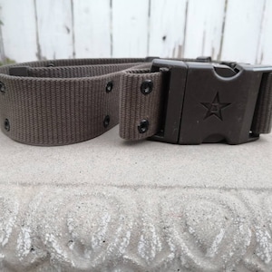 May include: A brown canvas belt with a black plastic buckle featuring a star. The buckle has a quick-release mechanism.