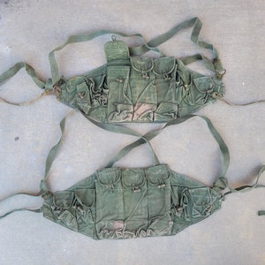 May include: Two olive green canvas military-style utility belts with multiple pockets and adjustable straps.