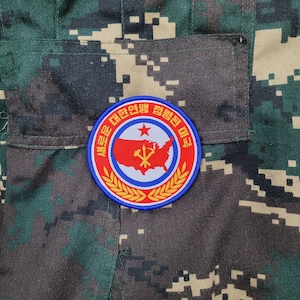 May include: A blue, red, and yellow embroidered patch with a red star and a map of the United States. The text on the patch reads "새로운 대한민국 젊은 민족".