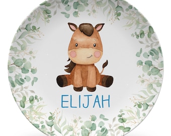 May include: A 10 inch plate featuring a watercolor illustration of a brown horse sitting in the center. The plate is decorated with a border of green eucalyptus leaves and branches. The name ELIJAH is printed in blue capital letters below the horse.