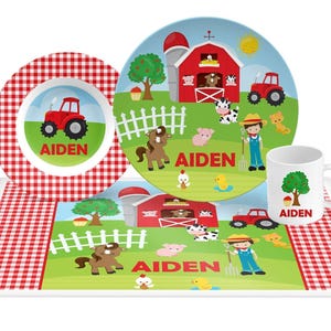 May include: A dinnerware set featuring a bowl, plate, mug, and placemat, all decorated with a farm scene including a red barn, tractor, animals, and the name AIDEN in red text. The items feature red and white gingham borders and green grass.