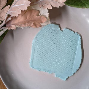 May include: A light blue silicone mould with a repeating pattern of small circles. The mould is on a light pink plate.