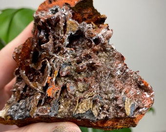 May include: A close-up of a mineral specimen with a rough, textured surface. The rock features a mix of rusty orange, brown, silver, and gray colors. The mineral appears to have a crystalline structure with some areas that look like they are covered in ice.