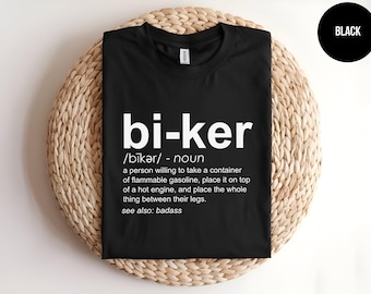 May include: A black t-shirt featuring white text that defines the word biker as a person willing to take a container of flammable gasoline, place it on top of a hot engine, and place the whole thing between their legs, with see also: badass.