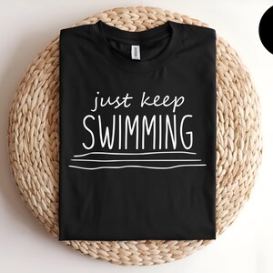 May include: Black t-shirt with white text that reads "just keep swimming" and three white lines underneath.