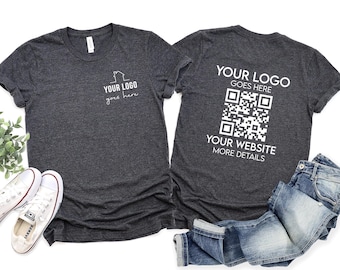 May include: Two dark heather gray t-shirts featuring white custom printing. The left shirt displays a small house icon with the text YOUR LOGO goes here. The right shirt features the text YOUR LOGO GOES HERE, a QR code, and YOUR WEBSITE MORE DETAILS.