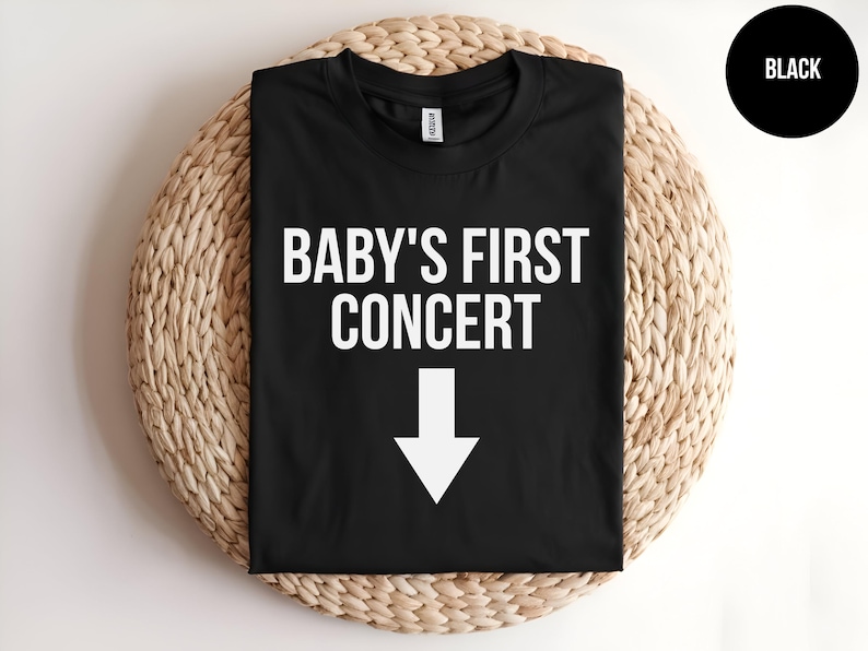 Pode incluir: Camiseta preta com texto branco que diz "BABY'S FIRST CONCERT" com uma seta branca apontando para baixo.