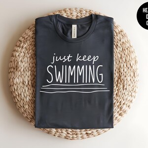 May include: Heather dark grey t-shirt with the text "just keep swimming" in white.