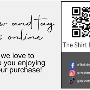 May include: A white card with black text that says "follow and tag us online" and "we love to see you enjoying your purchase!"  A black and white QR code is in the upper right corner of the card. Below the QR code is the text "The Shirt Republic". Below that is a black rectangle with three social media icons: Facebook, Instagram, and TikTok. The text below each icon is: "@TheShirtRepublicCo", "@theshirtrepubliccom", and "@theshirtrepublic".