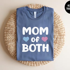May include: A blue t-shirt with the text "MOM of BOTH" in white, with a blue heart and a pink heart on either side of the word "of".