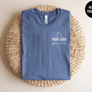 May include: A heather true royal blue t-shirt with a white outline of a house and the text "YOUR LOGO goes here".