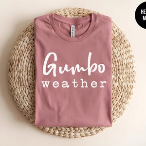 May include: A heather mauve t-shirt with the text "Gumbo weather" printed in white.