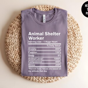 May include: A purple t-shirt with a white graphic that reads "Animal Shelter Worker" and lists the daily value of anxiety, passion, sleep, animal lover, compassion, and stress. The graphic is styled like a nutrition label.