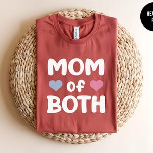 May include: Heather red t-shirt with the text "MOM of BOTH" in white with a blue heart and a pink heart.