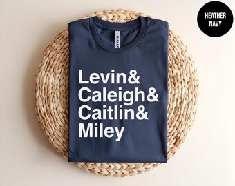 May include: A heather navy t-shirt featuring white text printed on the front that reads Levin & Caleigh & Caitlin & Miley. The shirt has a crew neckline and short sleeves, with a black circular badge in the corner labelled Heather Navy.