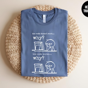 May include: A heather true royal blue t-shirt with a white graphic of a stick figure at a computer. The text on the shirt reads "the code doesn't work... why?" and "the code works... why?"