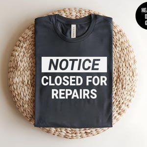 May include: Heather dark grey t-shirt with white text that reads "NOTICE CLOSED FOR REPAIRS".