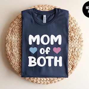 May include: A heather navy blue t-shirt with the text "MOM of BOTH" in white, with a blue heart and a pink heart on either side of the word "of".