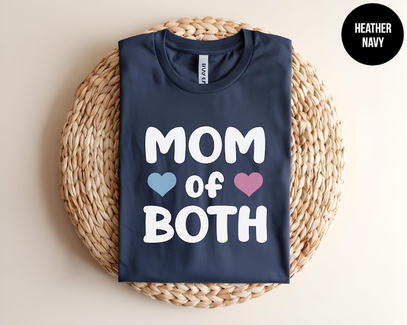May include: A heather navy blue t-shirt with the text "MOM of BOTH" in white, with a blue heart and a pink heart on either side of the word "of".