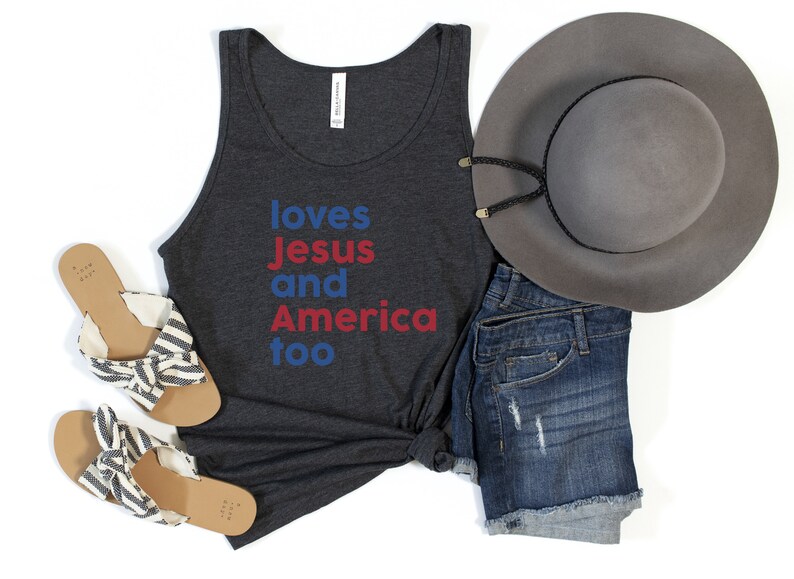 May include: A dark gray tank top with the words "loves Jesus and America too" in blue and red. The image also includes denim shorts, a gray hat, and striped sandals.