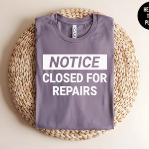 May include: A heather purple t-shirt with the text "NOTICE CLOSED FOR REPAIRS" in white.