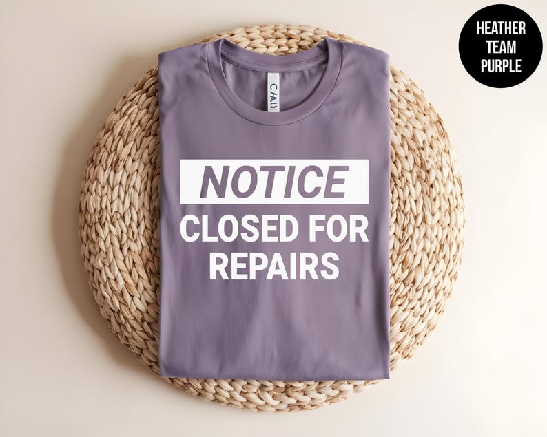 May include: A heather purple t-shirt with the text "NOTICE CLOSED FOR REPAIRS" in white.