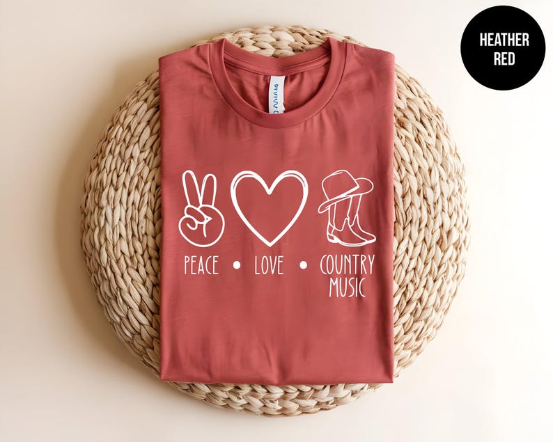 May include: A heather red t-shirt with a white peace sign, heart, cowboy hat, and boots graphic. The text "Peace. Love. Country Music" is printed below the graphic.