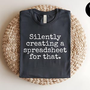 May include: Heather dark grey t-shirt with the text "Silently creating a spreadsheet for that."