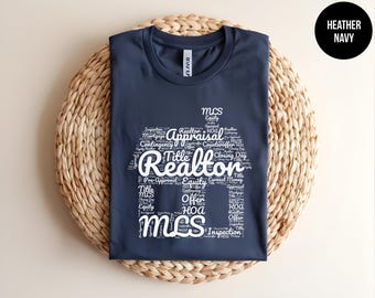 May include: A navy blue t-shirt featuring a white graphic print in the shape of a house. The graphic is composed of various real estate terms including Realtor, Appraisal, Title, Equity, Offer, HOA, and MLS. A black circle in the corner says HEATHER NAVY.