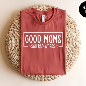 May include: Heather red t-shirt with the text "Good Moms Say Bad Words" printed in white.