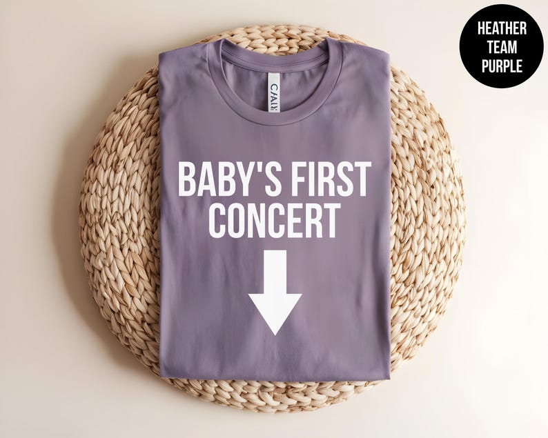 Pode incluir: Camiseta roxa em helanca com o texto "BABY'S FIRST CONCERT" e uma seta branca apontando para baixo.