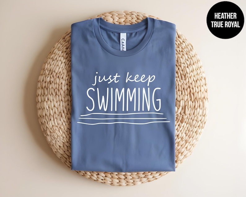 May include: A blue t-shirt with the text "just keep swimming" in white lettering. The shirt is on a woven straw surface.
