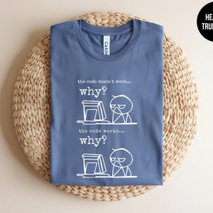 May include: A heather true royal blue t-shirt featuring a white graphic of a stick figure at a computer. The text reads: the code doesn't work... why? the code works... why? The design depicts the same frustrated figure in both scenarios.