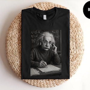 May include: Black t-shirt featuring a black and white image of Albert Einstein writing. The image includes equations and the text "E=mc²". The shirt has a crew neck and short sleeves. A black circle with the word "BLACK" is in the upper right corner.