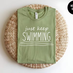 May include: A heather green t-shirt with the text "just keep swimming" in white.