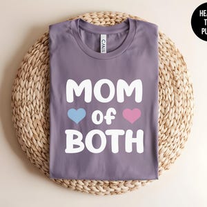May include: Purple heather t-shirt with the text "MOM of BOTH" in white with a blue and pink heart on either side of the word "of".