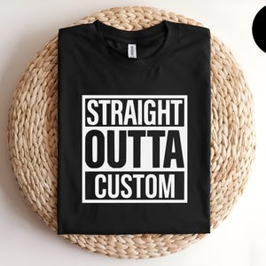May include: A black short-sleeved t-shirt featuring a white square graphic on the chest. Inside the square, the text reads STRAIGHT OUTTA CUSTOM in bold, capitalized, sans-serif lettering. The shirt has a crew neckline and a standard fit.