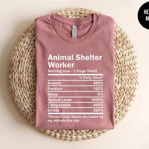 May include: A heather mauve t-shirt with the text "Animal Shelter Worker" and a nutrition facts style graphic listing the percentage of daily value for anxiety, passion, sleep, animal lover, compassion, and stress. The text at the bottom reads "*Percent Daily Values are based on my attitude that day."