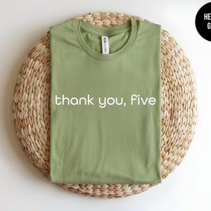 May include: A heather green t-shirt with the text "thank you, five" printed in white.