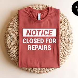 May include: Heather red t-shirt with a white graphic that says "NOTICE CLOSED FOR REPAIRS".