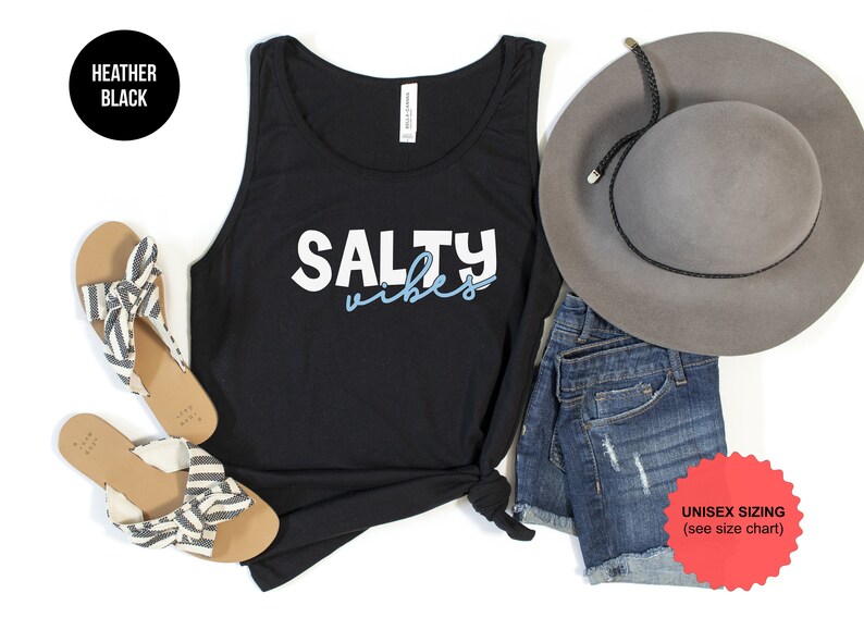 May include: Black tank top with the text "Salty Vibes" in white and blue lettering. The tank top is styled with denim shorts, a gray hat, and striped sandals.
