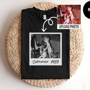 May include: Black t-shirt featuring a black and white photo in a white frame. The photo shows a child on a rocking horse. The text "Summer 1980" is below the photo. A smaller color photo is in the upper right corner, with the text "UPLOAD PHOTO".