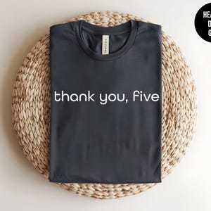 May include: Heather dark grey t-shirt with the text "thank you, five" printed in white.