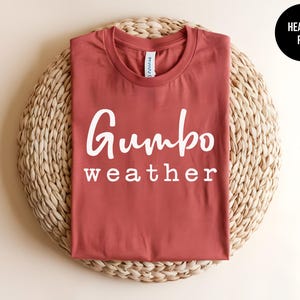 May include: A heather red t-shirt with the text "Gumbo weather" printed in white on the front.