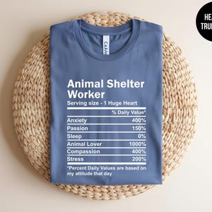 May include: A blue t-shirt with white text that reads "Animal Shelter Worker" and a nutrition label listing the daily value of anxiety, passion, sleep, animal lover, compassion, and stress. The text at the bottom reads "*Percent Daily Values are based on my attitude that day"