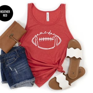 May include: A red heather tank top with a white graphic of a football and the text 'game day'. The tank top is paired with denim shorts and white sandals.