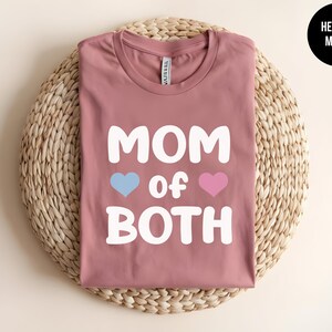May include: Heather mauve t-shirt with the text "Mom of Both" in white, featuring a blue heart and a pink heart.
