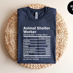 May include: A navy blue t-shirt with white text that reads "Animal Shelter Worker" and a nutrition facts label listing "Anxiety", "Passion", "Sleep", "Animal Lover", "Compassion", and "Stress" with percentages next to each item.